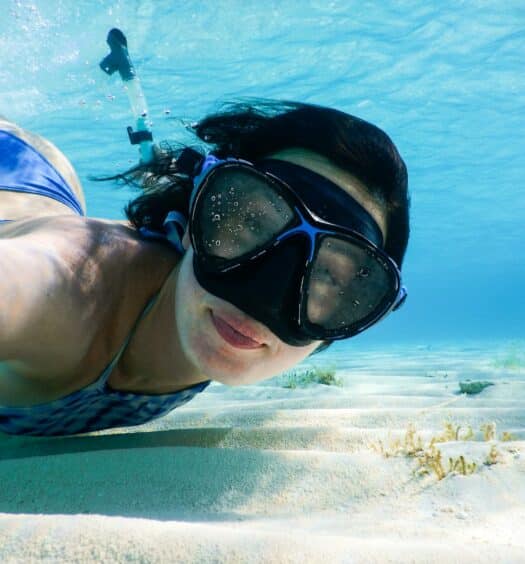 Mulher de biquíni azul tirando selfie embaixo d'água com uma máscara de mergulho no rosto.