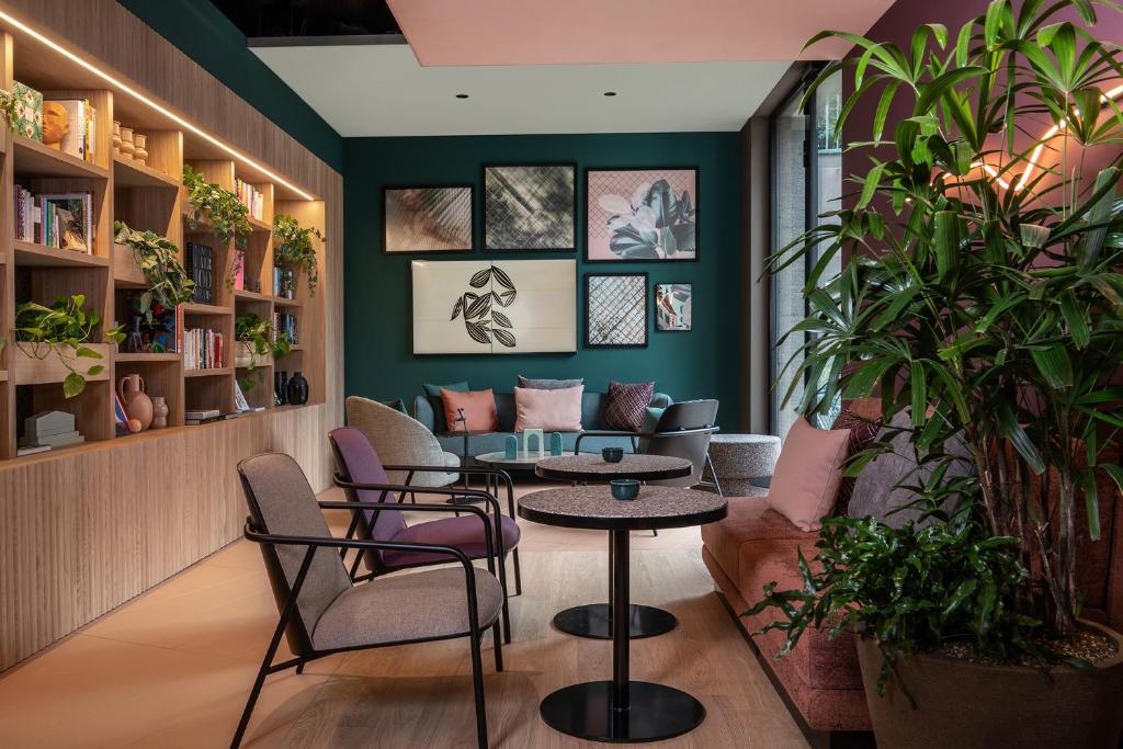 Área comum do Sorell Hotel St. Peter, em Zurique, com uma parede verde turquesa escura, com alguns quadros pendurados, um sofá no mesmo tom na frente, uma parede com livros e mesas redondas com cadeiras para os hóspedes