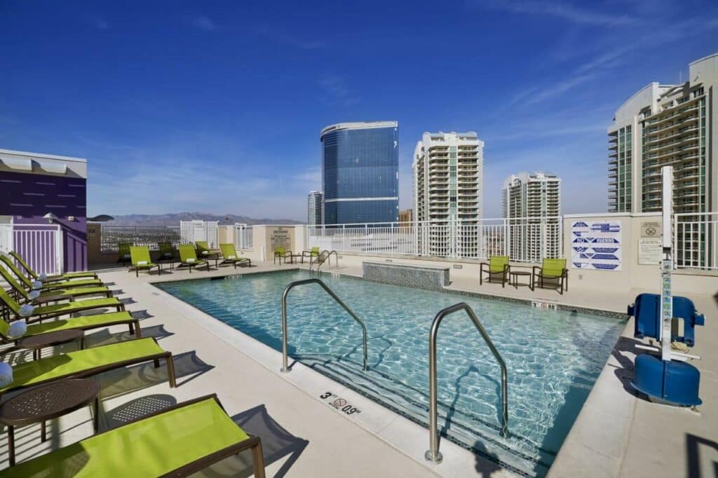 Piscina na cobertura do SpringHill Suites by Marriott Las Vegas Convention Center com barras de apoio e escada para entrar na piscina, ao redor da piscina há um deck com espreguiçadeiras verde, e no local dá para ver diversos prédios
