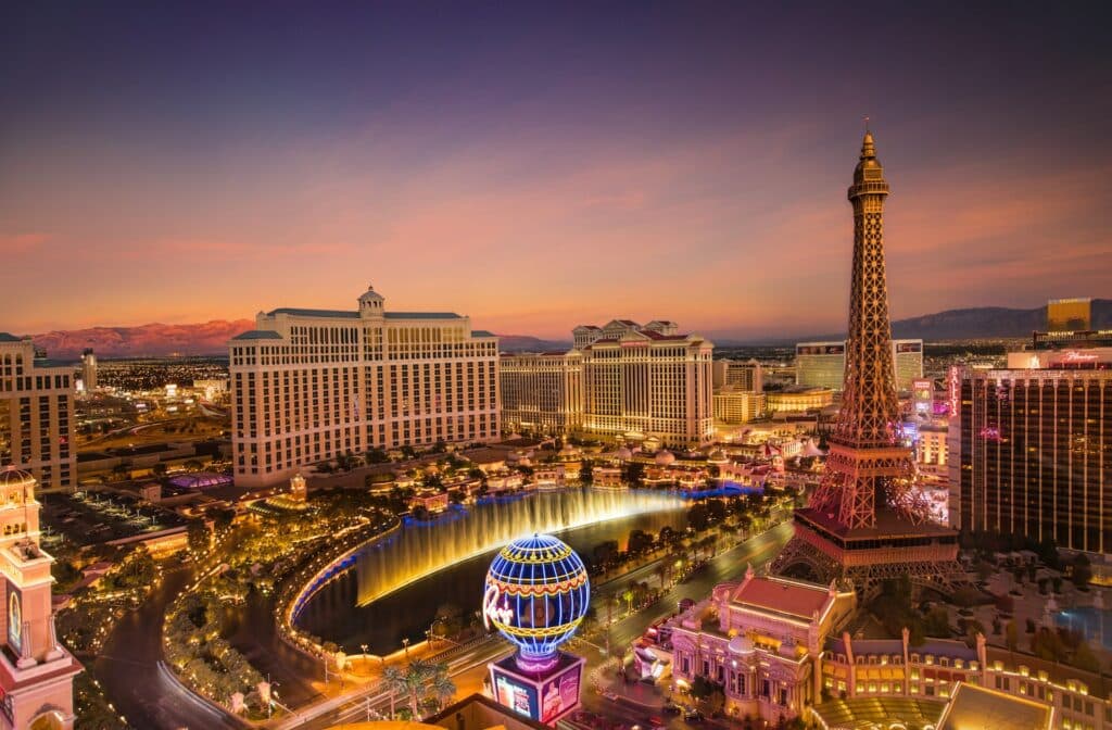 Visão aérea de Las Vegas Strip com um enorme lago iluminado, muitos hotéis ao redor, ruas movimentadas, tudo muito iluminado durante à noite