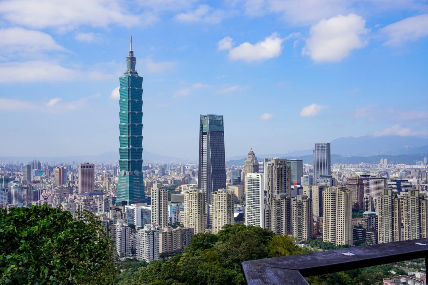 Cidade de Taipei com prédios ao entorno de natureza exuberante e céu azul com nuvens