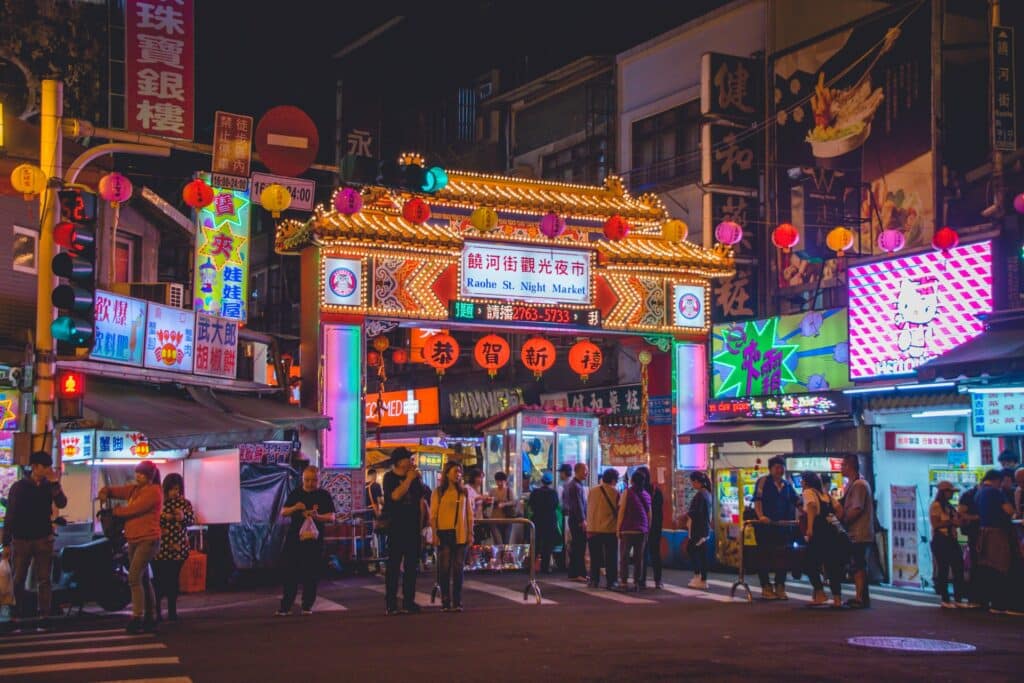 Grupo de pessoas em Taiwan no mercado de Raohe de noite, luzes de comércios e decorações típicas.