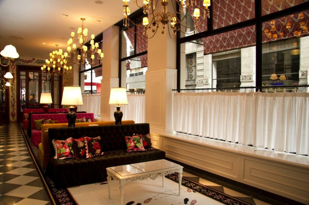 Restaurante do Tango de Mayo Hotel com sofás, amplas janelas com cortinas, lustres com muitas lâmpadas, alguns abajures entre os sofás, tudo em tons de branco, preto e detalhes em rosa
