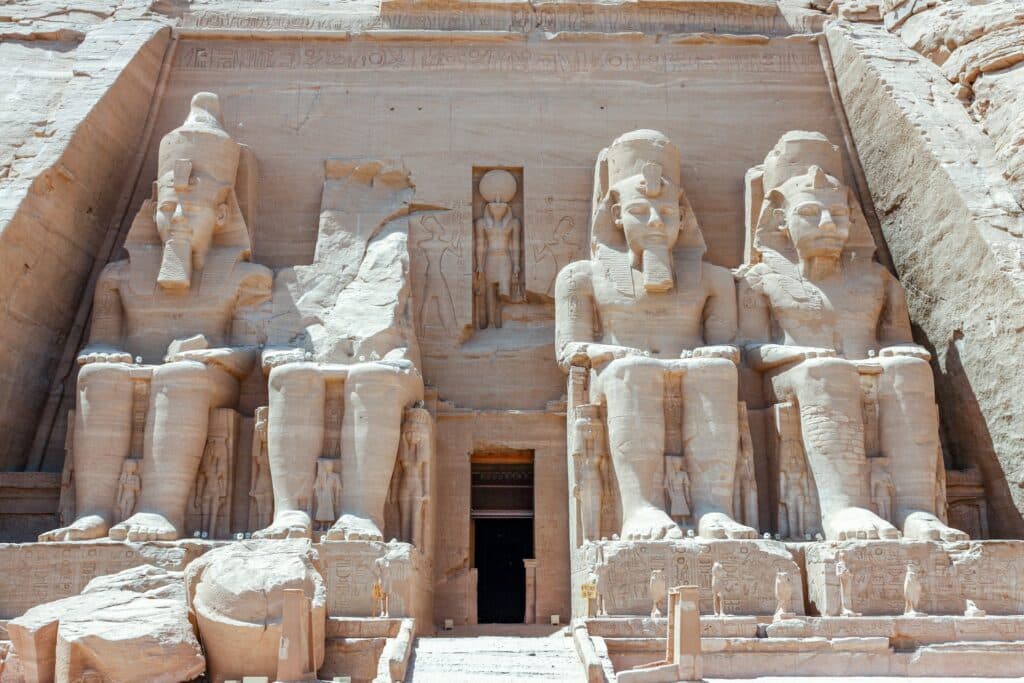 fachada do templo com quatro estátuas de faraó sentados esculpidos em pedra, com a entrada no meio e uma estátua de pé, bem menor, no centro, também representando um faraó, em Abu Simbel, representando o post de chip celular Egito