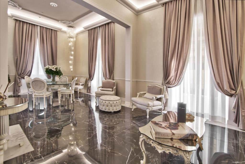 Área comum do The Moon Boutique Hotel & Spa, em Florença, com chão de mármore refletindo a luz do dia saindo das janelas, com móveis de época, incluindo mesa redonda com cadeiras, poltronas, vaso de flor, lustre suspenso e cortinas altas e elegantes
