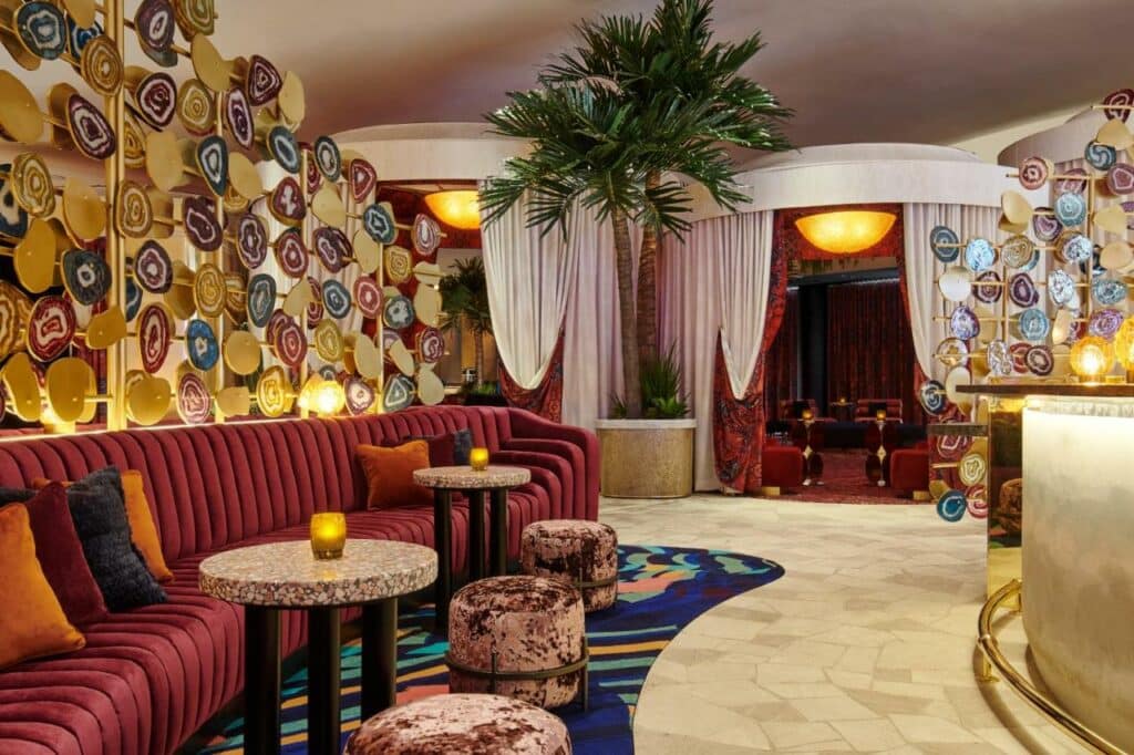 Parte interna do Virgin Hotels Las Vegas, Curio Collection by Hilton com sofás em tom de vinho e almofadas coloridas, alguns pufes redondos, o local é decorado em tons de vinho e azul