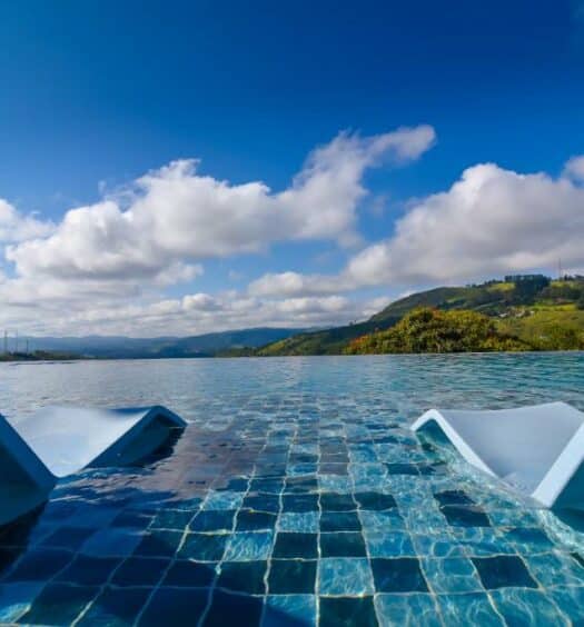 duas espreguiçadeiras dentro da piscina no Hotel Refúgio Vista Serrana com vista para as montanhas com céu azul e muitas nuvens no Hotel Refúgio Vista Serrana, em Mairiporã