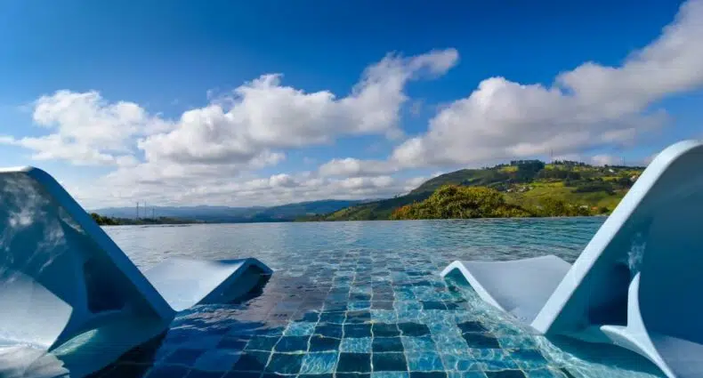 duas espreguiçadeiras dentro da piscina no Hotel Refúgio Vista Serrana com vista para as montanhas com céu azul e muitas nuvens no Hotel Refúgio Vista Serrana, em Mairiporã
