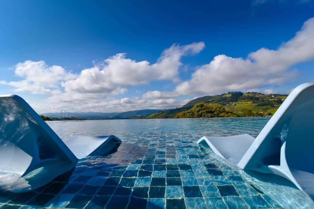 duas espreguiçadeiras dentro da piscina no Hotel Refúgio Vista Serrana com vista para as montanhas com céu azul e muitas nuvens no Hotel Refúgio Vista Serrana, em Mairiporã