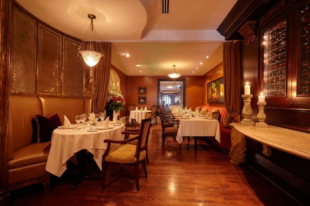Salão do restaurante do Wedgewood Hotel & Spa - Relais & Chateaux em estilo de época com tudo decorado em madeira, as mesas são redondas e com cadeiras de madeira acolchoadas em bege, o chão também é de madeira e há alguns lustres redondos pelo ambiente