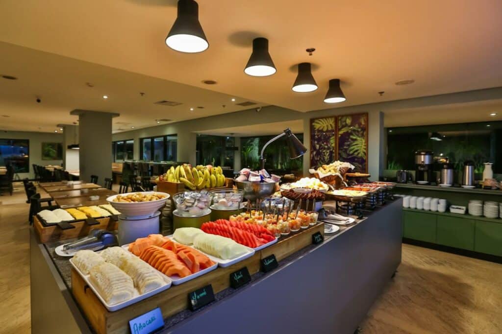 Área de refeições do Wyndham São Paulo Berrini com uma bancada com frutas e pães disponíveis