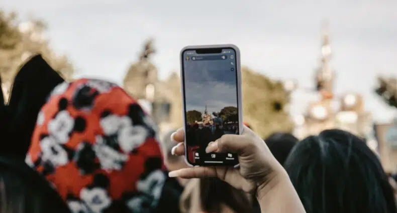Uma pessoa segurando um celular em direção de um castelo na Disney