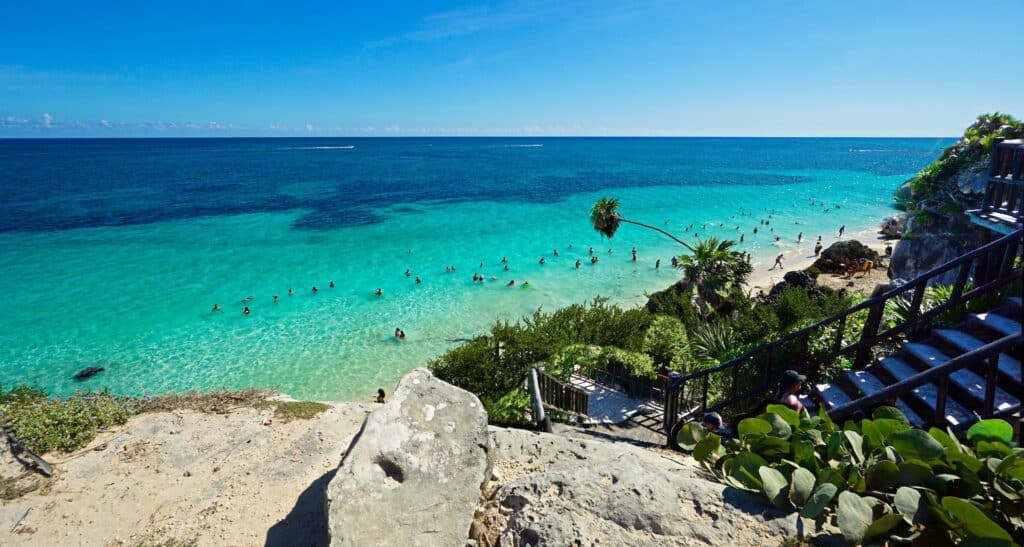 escada que desce para a praia com alguma vegetação e um mar de tons verdes e azuis com pessoas se banhando em Tulum, Quintana Roo no México, para ilustrar o post de chip celular Caribe