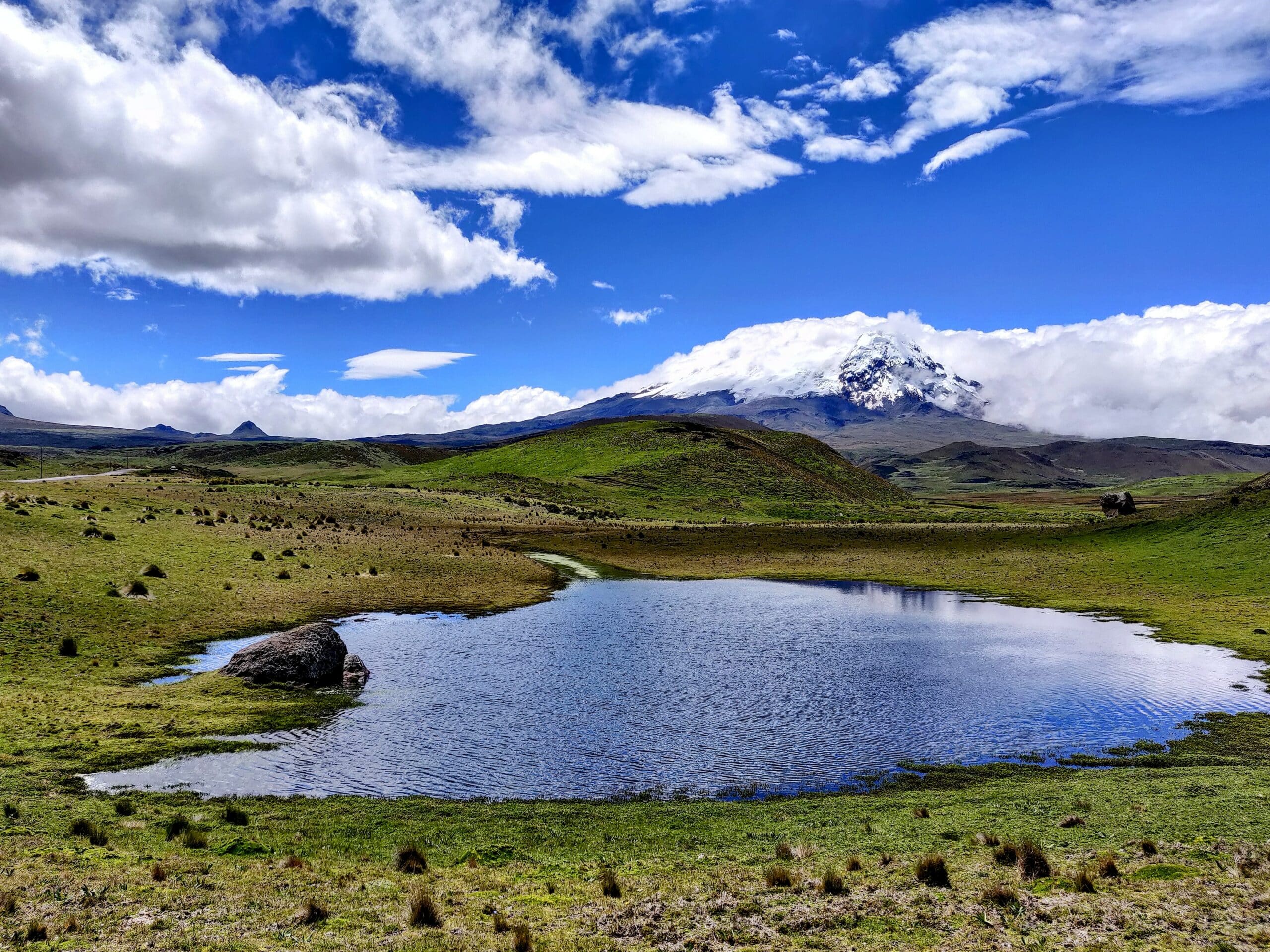 Vista da região do Antisana, Equador com lago, vegetação em volta, montanhas e vulcão ao fundo, com céu claro e nuvens brancas. Representa chip celular Equador