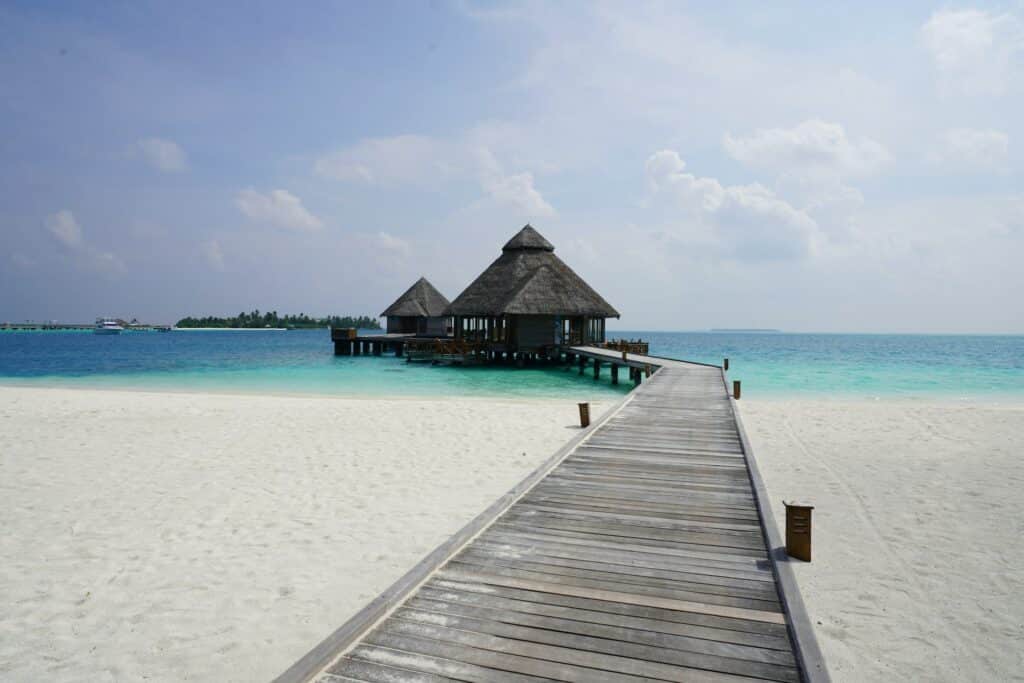 ponte de madeira que sai da praia de areias brancas até o mar de águas azuis claras e, ao final, alguns bangalôs no Atol Alif Alif, para ilustrar o post de chip celular Maldivas