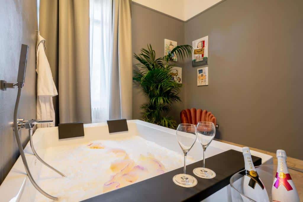 banheira grande do The Rif - Boutique Hotel, um dos hotéis em Pisa, com espaço para duas pessoas, champanhe e poltrona, uma janela com cortina e plantinhas