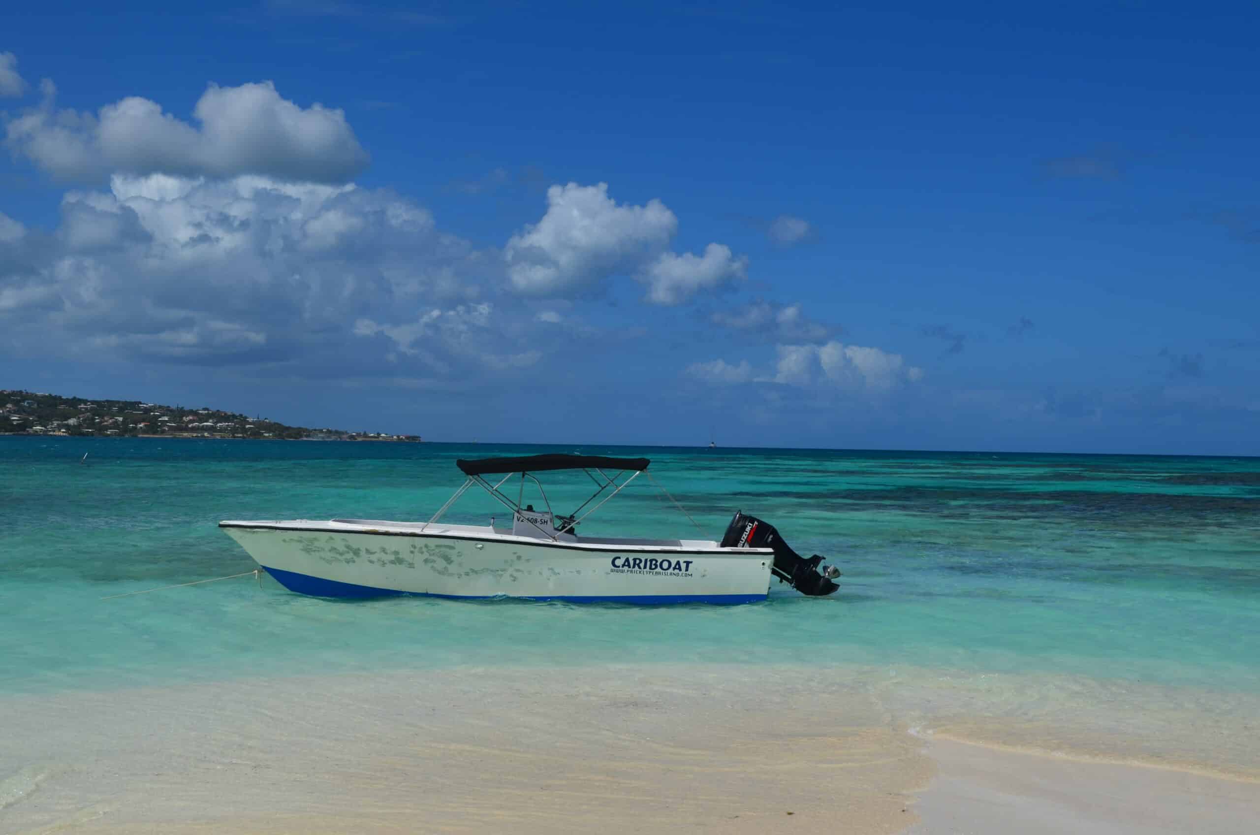 Barco simples, branco, no mar turquesa da Ilha St Martin em dia ensolarado, de céu azulado e com poucas nuvens