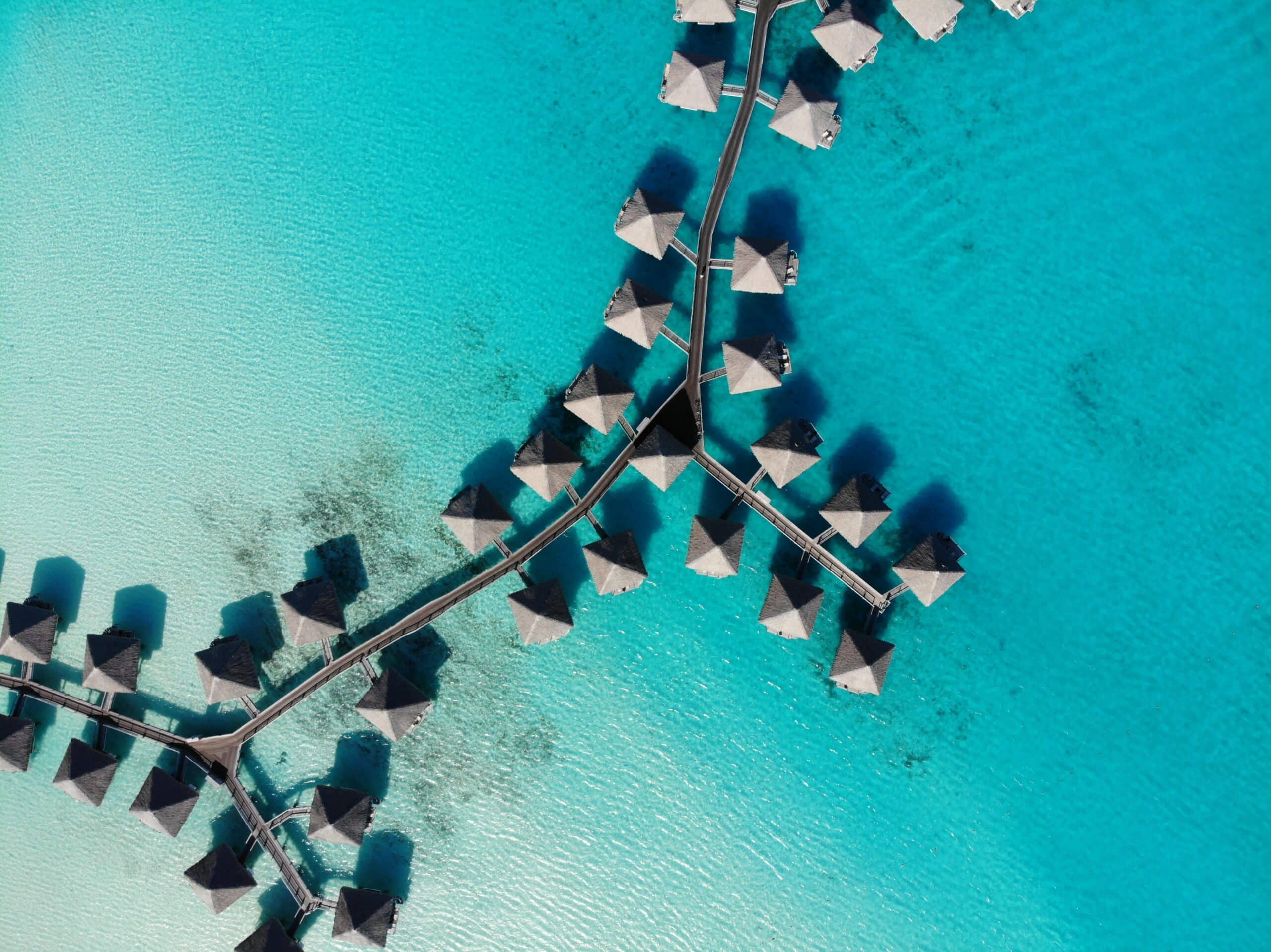 Vista de cima de Bora Bora, Polinésia Francesa com cabanas em cima do mar azul em dia de sol.