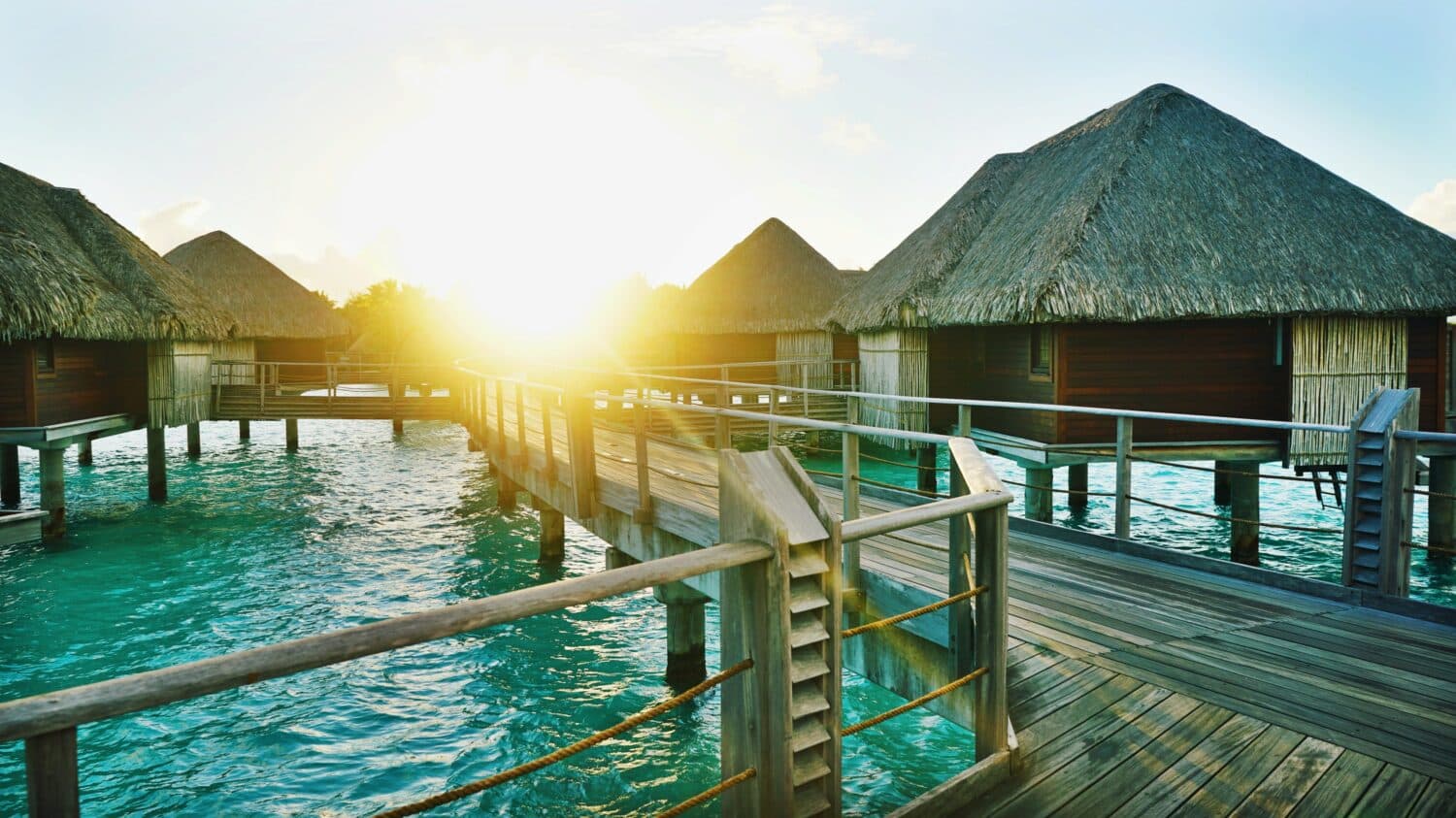 Vista do nascer do sol em Bora Bora, na Polinésia Francesa, com cabanas em cima do mar, ponte de madeira que liga elas e mar verde. Representa chip celular Bora Bora