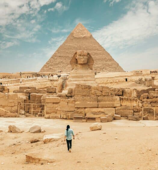 Vista da frente das pirâmides de gizé em Cairo, Egito com um homem caminhando até o monumento durante o dia.