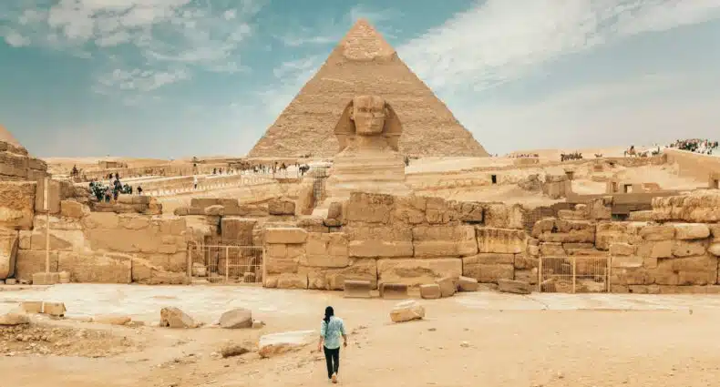Vista da frente das pirâmides de gizé em Cairo, Egito com um homem caminhando até o monumento durante o dia.
