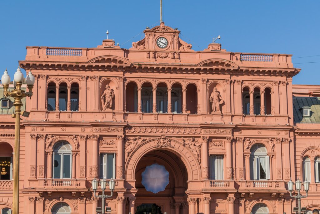 Construção rosada com colunas, estátuas e um relógio no topo para ilustrar o post sobre chip de celular para Buenos Aires. Acima, o céu é azul e a foto foi tirada de dia. - Foto: Patricio ASC via Unsplash
