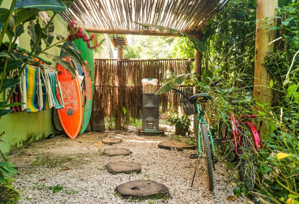 Quintal do Casa Viva Itamambuca com muito verde ao redor, pranchas de surf e cadeiras de praia penduradas, além de duas bicicletas