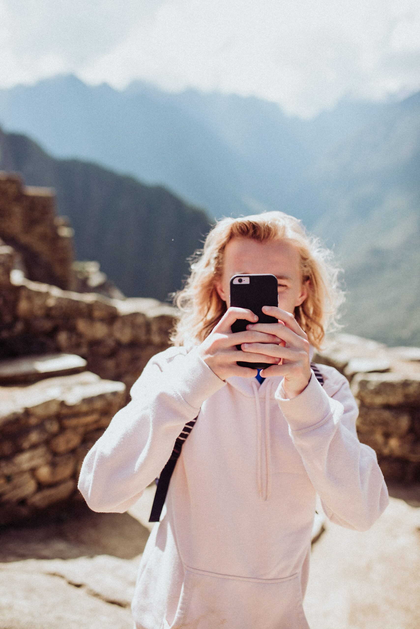 Homem loiro com celular na mão tirando foto em Machu Picchu no Peru. Representa chip celular Peru