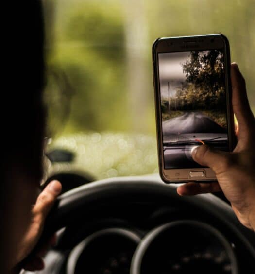 Homem com celular na mão dentro do carro tirando foto de paisagem em Quito. Representa chip celular Equador