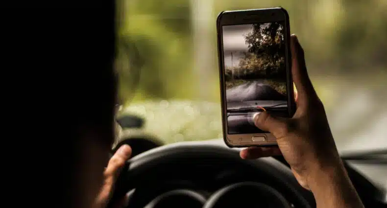 Homem com celular na mão dentro do carro tirando foto de paisagem em Quito. Representa chip celular Equador