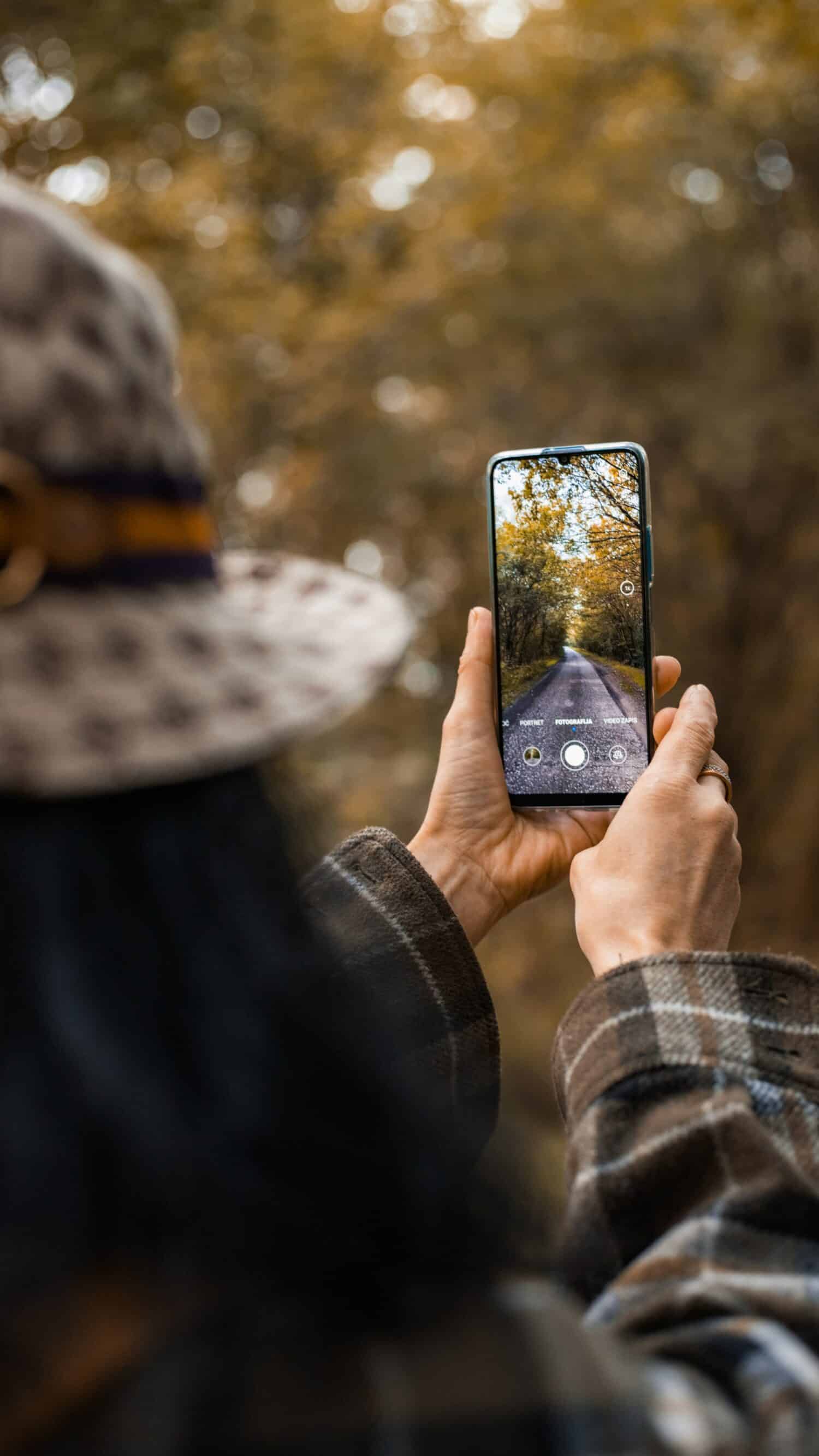 Mulher segurando o celular na mão fotografando alguma paisagem. Representa chip celular Sérvia