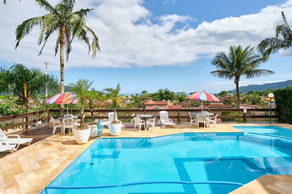 Piscina do Chalés Mirante da Lagoinha com um deck que dá vista para árvores, montanhas e a praia mais ao fundo. Representa airbnb na praia do Tenório.