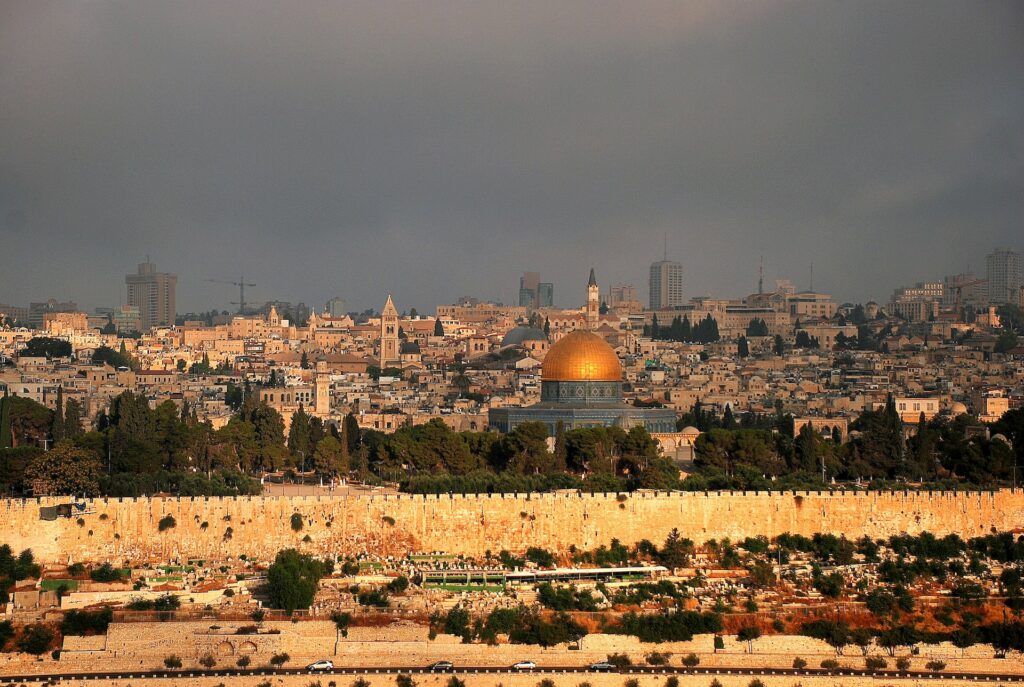 Cidade de Jerusalém vista de cima, com construções, prédios, casa e vegetação ao entorno. Edifícios históricos, um com uma cúpula dourada reluzente e céu azul para representar o seguro viagem Jerusalém.