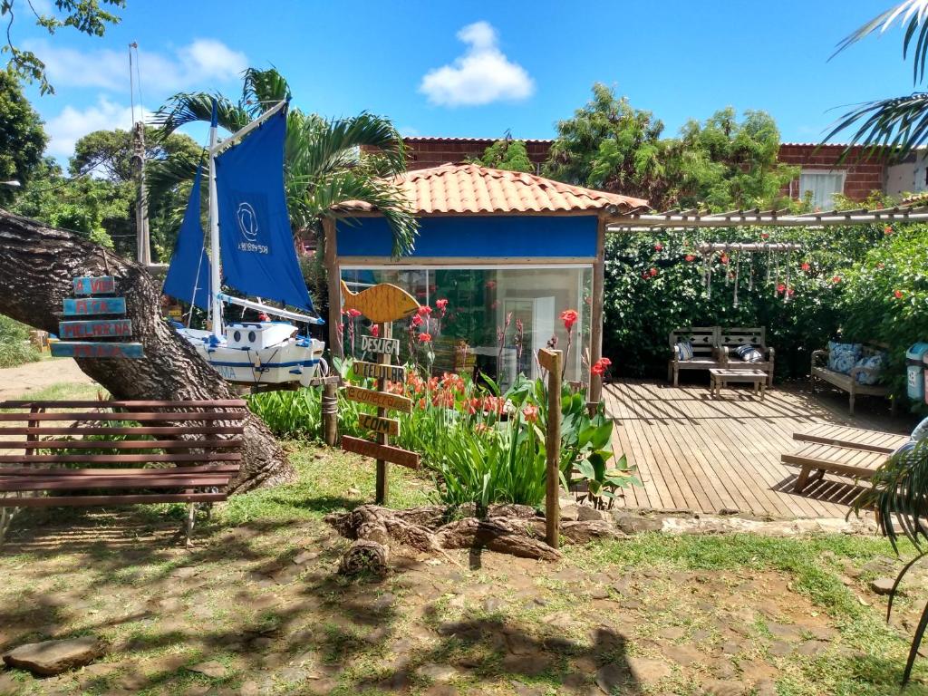 Área externa da Corrente Marítima Pousada, em Fernando de Noronha, com banco de madeira ao ar livre, deck, espreguiçadeiras, e uma casinha com paredes azuis, além de canteiro com flores