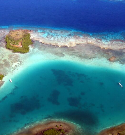 Vista aérea de uma pequena ilhota cercada pelo mar de azul claro e verde