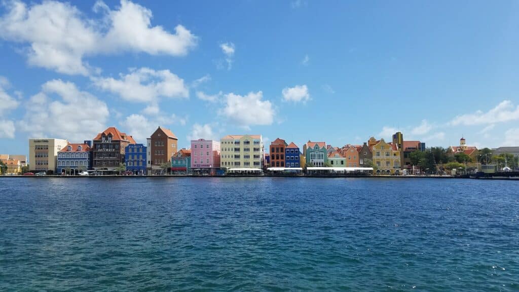 Alguns prédios coloridos de Curaçao, virados em direção ao mar azul escuro, em um dia de céu claro com poucas nuvens