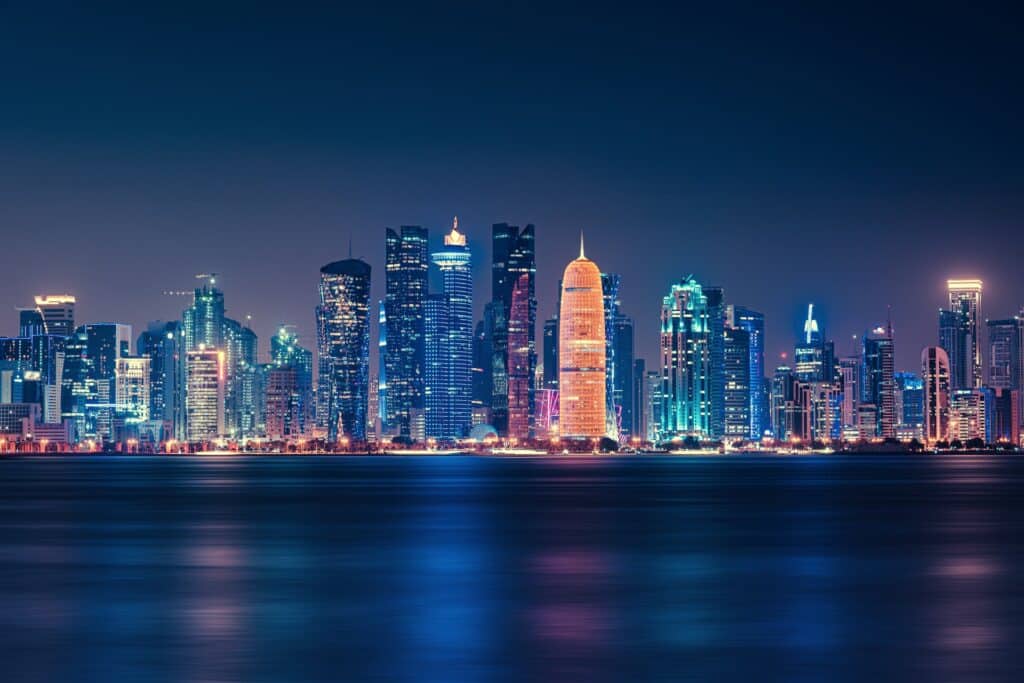 Arranha-céus iluminados em frente ao mar que reflete as luzes dos prédios. - Foto: Abdullah Ghatasheh via Pexels
