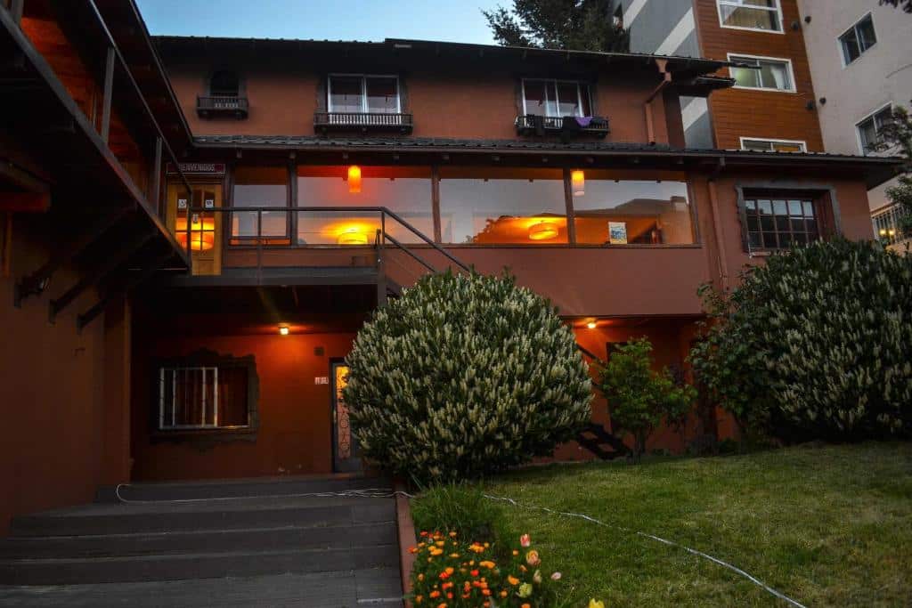 Frente do Hostel Inn Bariloche com cores marrom avermelhado, janelas de vidro, árvores na frente.