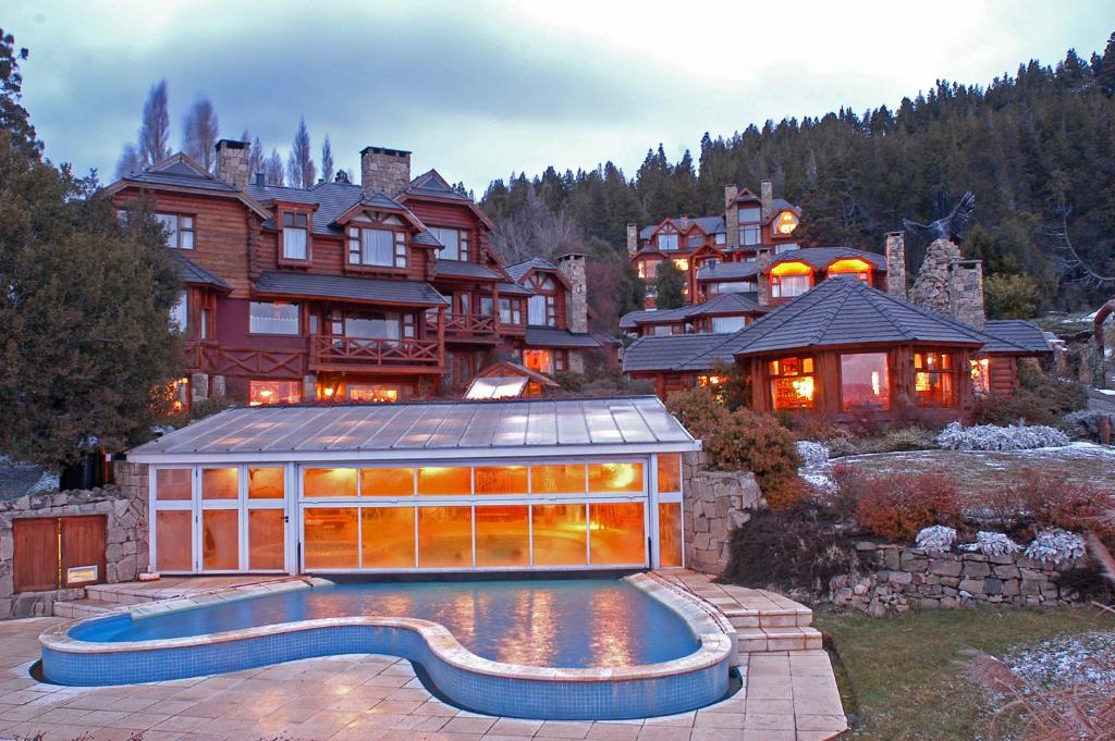 Visto do Nido del Cóndor Hotel & Spa com piscina a frente e ao fundo a hospedagem e ao fundo árvores. Representa hotéis em Bariloche