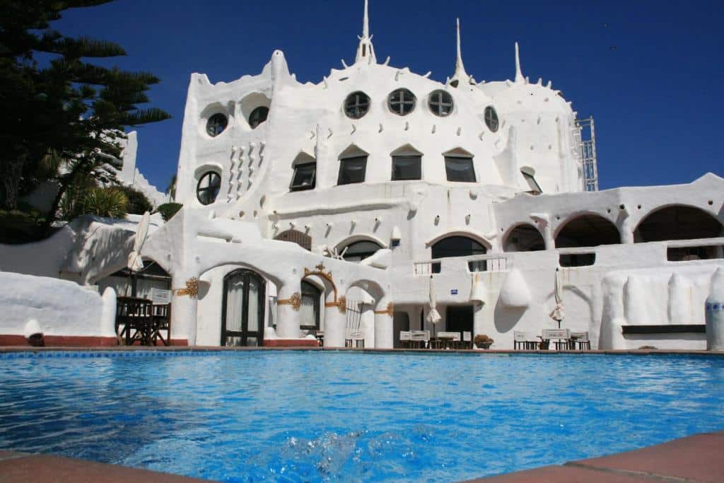 Vista do Club Hotel Casapueblo com arquitetura mediterrânea de cor branca, várias janelas e piscina a frente da estadia. Representa hotéis em Punta Del Este.