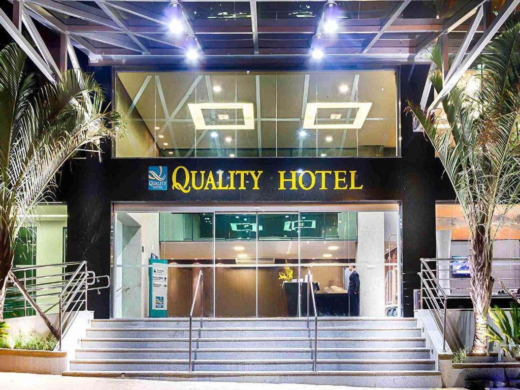 Frente do Quality Hotel Pampulha & Convention Center com portas de vidro e janelas durante a noite e duas árvores em cada lado da entrada