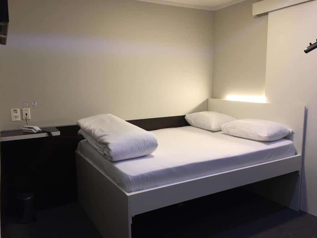 Uma cama de casal pequena com dois travesseiros e um edredom branco no Hotel Aero Sleep Campinas, para representar hotéis perto do Aeroporto de Viracopos em Campinas