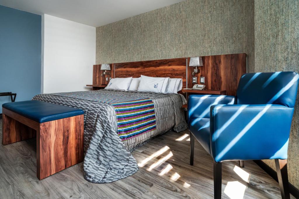 Quarto do Hotel Parque Satelite, com uma cama de casal, com cabeceira de madeira, contendo um abajur de cada lado, tomadas e telefone ao lado, além de uma poltrona azul
