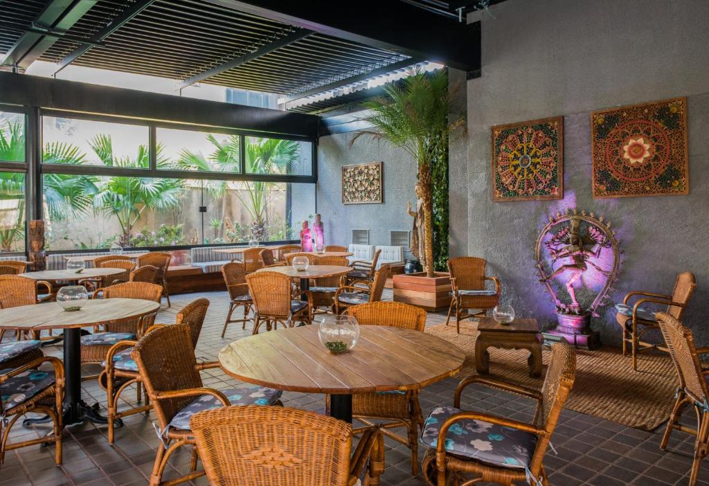 Área de refeições no Hotel Transamerica Berrini com mesas e cadeiras de madeira, decoração rústica com elementos em palha e algumas plantas