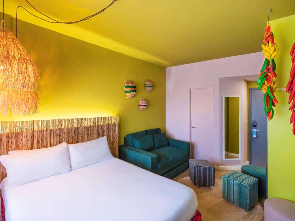 Quarto do ibis Styles Sao Paulo Barra Funda com paredes em tom de verde abacate, uma cama de casal, uma sofá de dois lugares verde escuro, um espelho de corpo inteiro e alguns bufês também verdes pelo ambiente