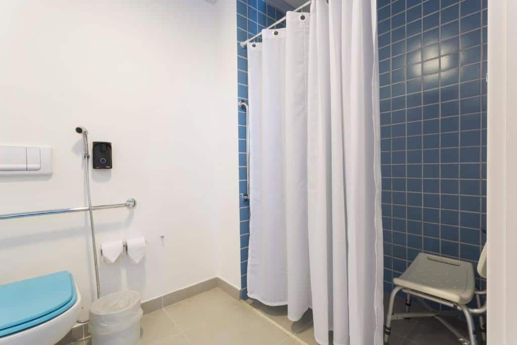 Banheiro adaptado do ibis Styles Sao Paulo Barra Funda com barras de apoio perto da privada e dentro do box, além de uma cadeira dentro do box que é de cortinas
