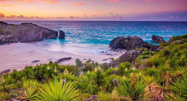 Vista do mar de Bermudas com areia branca, mar com tonalidade azul no pôr-do-sol. Representa chip celular Bermudas.
