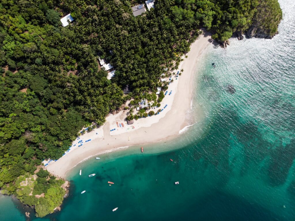 Vista aérea de uma praia para ilustrar o post sobre chip de celular para Costa Rica. O mar é turquesa com alguns barcos e há várias árvores perto da costa. - Foto: Atanas Malamov via Unsplash