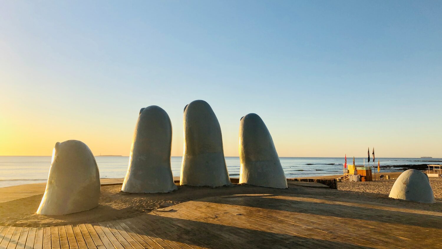 Vista do monumento La Mano, Punta del Este, com pontas dos dedos saindo do chão com vista para o mar no pôr-do-sol.