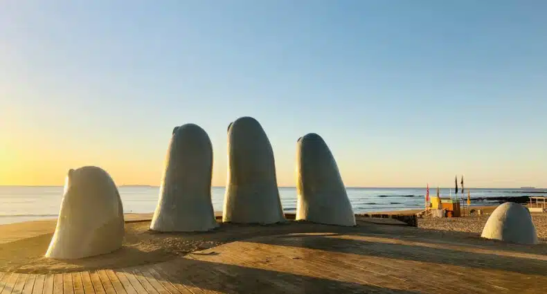 Vista do monumento La Mano, Punta del Este, com pontas dos dedos saindo do chão com vista para o mar no pôr-do-sol.